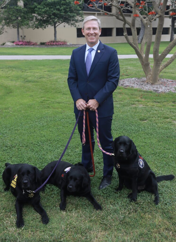 Photo of Erik Nasarenko with the courthouse dogs Star, Trakr, and Comet on a green lawn.
